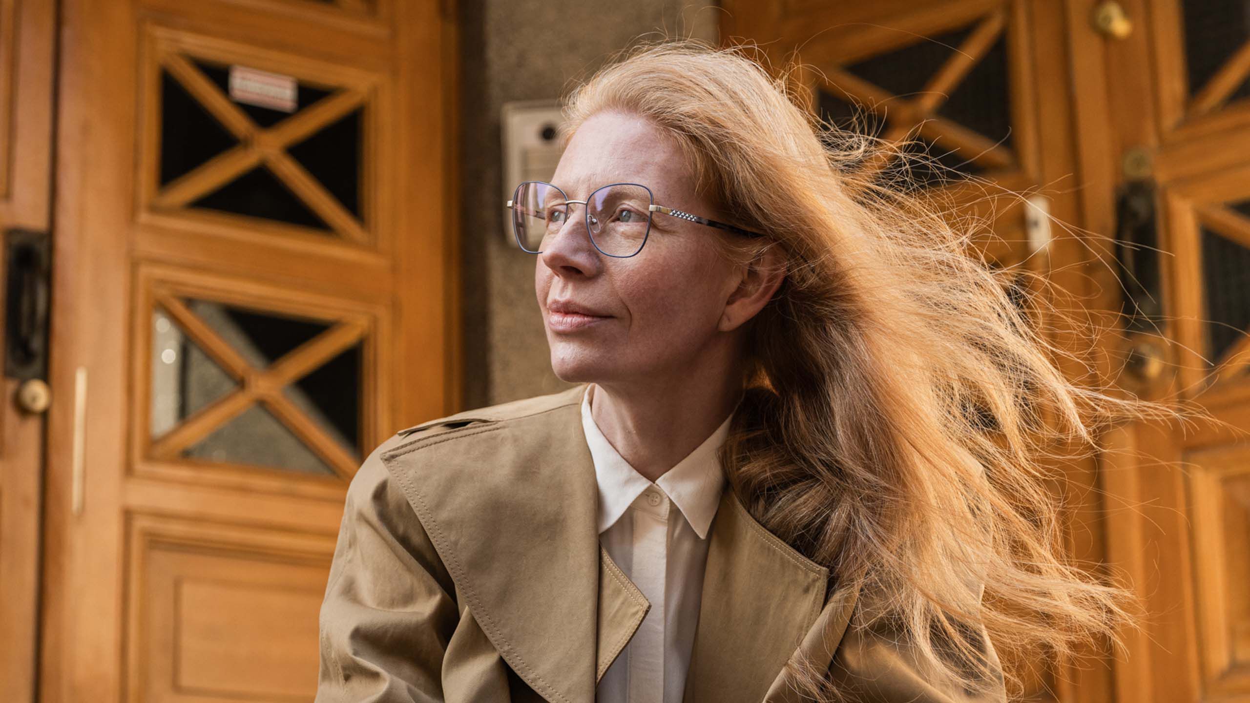 Mies seisoo luentosalissa, kahvikuppi kädessä, viltti olkapäällä ja pilottimalliset silmälasit kasvoillaan